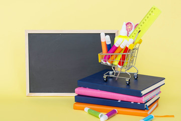 Back to school concept on yellow paper background. Basket with stationery. books. blackboard.