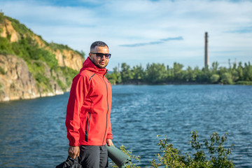 Photo of handsome smiling man in red coat in autumn or spring scenery at the quarry lake.
