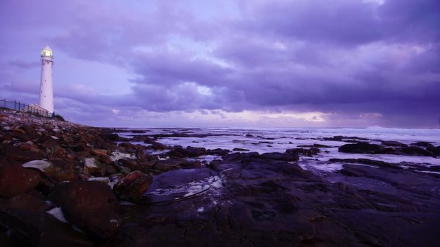Lighthouse on rocky shore with dramatic clouds rolling in.Time lapse