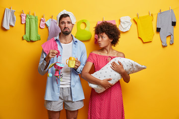 Female and male babysitters feel exhausted by noisy newborn. Husband, wife care about infant. Sad young father going to feed child, holds bottle of milk. Upset mommy cannot sooth crying baby