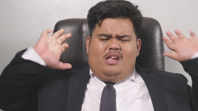 A funny Asian fat businessman wearing a suit look like the head of corporate executive or business manager is feeling tired and exhausted, rest until yawning because of hard work and less rest.