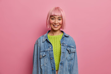 Portrait of good looking young woman with pink hairstyle, smiles gently, expresses positive...