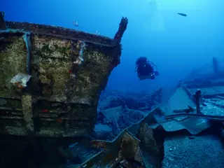 Fotobehang Schipbreuk scuba divers exploring shipwreck scenery underwater ship wreck deep blue water ocean scenery of metal underwater and fish around  © underocean