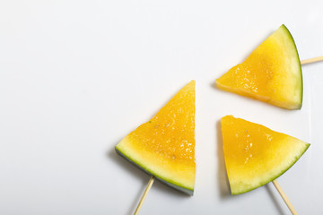 Pieces of yellow watermelon on sticks. Plate on a white surface.