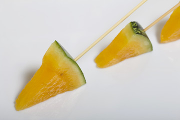 Pieces of yellow watermelon on sticks. Plate on a white surface.
