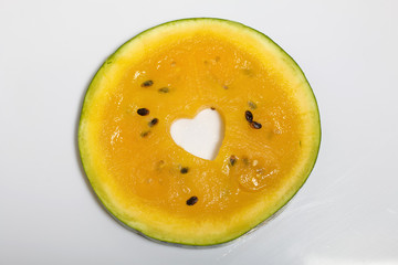 Slice of yellow watermelon on a white background. It has a heart-shaped hole in it.