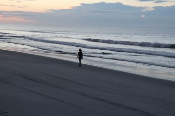 Twilight morning as lady walking in solitude on the beach and waves splashing against the shore