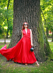 Attractive young girl, lady in long red dress in summer forest park, fashionable woman outdoors in nature