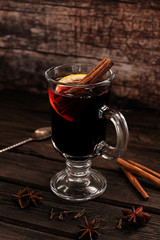 A glass of hot mulled wine with cinnamon sticks and a slice of lemon, on a dark vintage wooden background