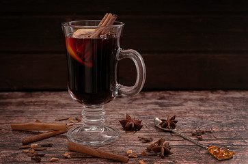 A glass of hot mulled wine with cinnamon sticks and a slice of lemon, on a dark vintage wooden background