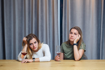 Two best friends. Young European-looking women having a conversation sitting at a desk holding a glass of wine. beautiful girls sisters love to drink alcohol laughing cheerful relax in the living room