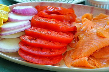 Platter of smoked salmon slices with tomatoes, onion, cheese, and toasted muffins