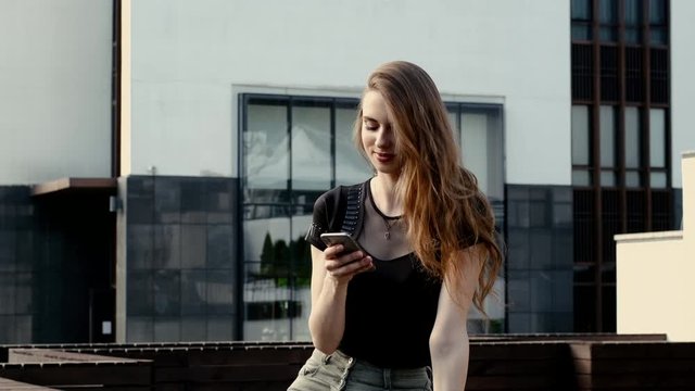 Cheerful young woman scrolling feed of social network on smartphone outdoor