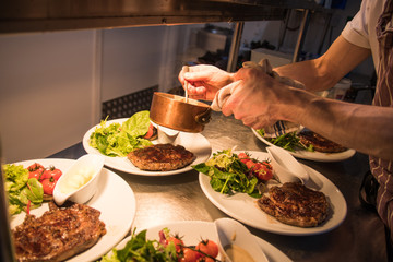 chef in the kitchen putting sauce on freshly cooked steak at the pass