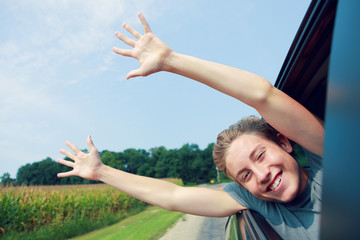 Boy putting his heads and hands out of the car window driving down a country road