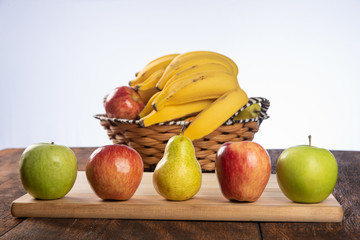 fruit basket with bananas, apples and oranges on polished wood, placed on rustic wood with selective focus.