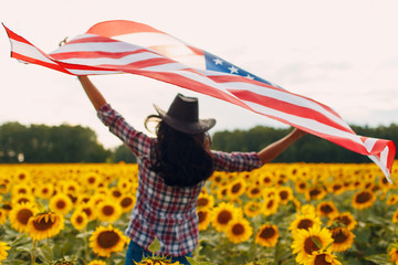 Young woman with American flag in the sunflower field. 4th of July Independence Day USA concept