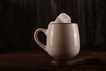 Marshmallows in a mug on a dark background close-up and copy space. Marshmallow in a cup with cocoa pattern top view in a dark key.
