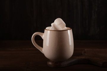 Marshmallows in a mug on a dark background close-up and copy space. Marshmallow in a cup with cocoa pattern top view in a dark key.