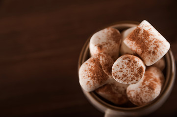 Marshmallows in a mug on a dark background close-up and copy space. Marshmallow in a cup with cocoa pattern top view in a dark key.