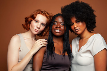 young pretty caucasian, afro, scandinavian woman posing cheerful together on brown background, lifestyle diverse nationality people concept