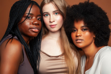 young pretty caucasian, afro, scandinavian woman posing cheerful together on brown background, lifestyle diverse nationality people concept