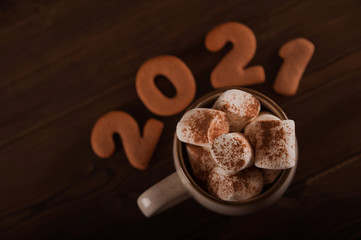 Inscription 2021 gingerbread cookie. Happy new year 2021 and marshmallows in a mug on a dark background close up and copy space. Marshmallow in a cup with gingerbread cookie pattern top view in a dark