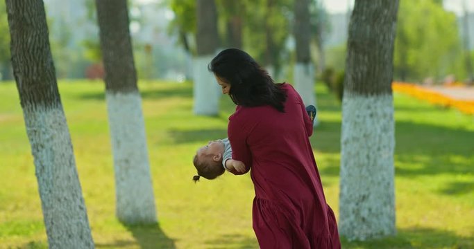 Happy mother shakes and circles the baby in her arms, cheerful childhood. Mom plays with the child in the park, holds him in her arms. 4k, 10bit, ProRes