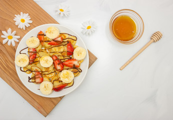Trendy food - pancake cereal. Heap of mini cereal pancakes on a white plate, copy space. Strawberries, bananas, and honey. A beautiful and healthy Breakfast. Top view.