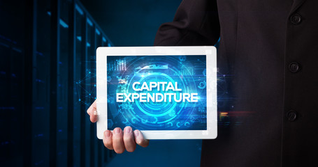 Young business person working on tablet and shows the inscription: CAPITAL EXPENDITURE, business concept