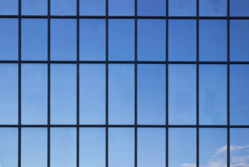 Windows in an office building, background. Blue sky reflected in the glass, black frames.
