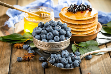 Blueberries in a plate and pancakes, on an old background.