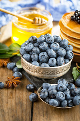 Blueberries in a plate and pancakes, on an old background.