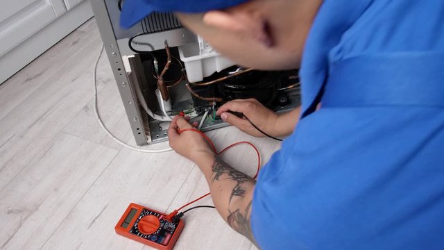 Worker repairing refrigerator in kitchen