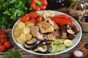 Fried chicken slices with potatoes,  bell peppers, eggplant, zucchini, cherry tomatoes, mushrooms and onions on a wooden background.