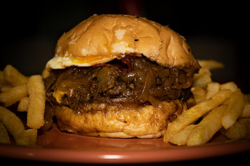 Tasty big burger with onions and egg. French fries in the dish.