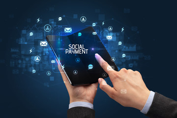 Businessman holding a foldable smartphone with SOCIAL PAYMENT inscription, social networking concept