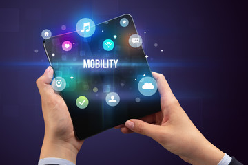 Businessman holding a foldable smartphone with MOBILITY inscription, social media concept