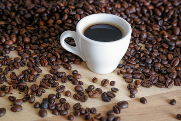  A cup of black coffee with coffee grains, natural light on wooden table