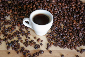  A cup of black coffee with coffee grains, natural light on wooden table