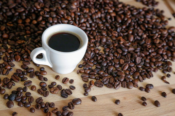 Coffee grains with white cup on coffee on wooden table, natural light