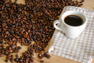 Coffee grains with white cup on coffee on wooden table, natural light