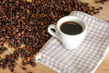 Coffee grains with white cup on coffee on wooden table, natural light
