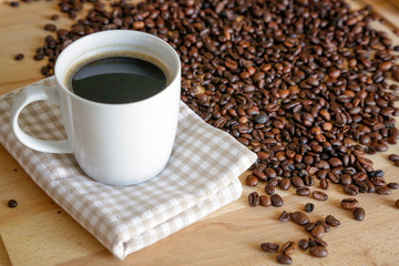 Coffee grains with white cup on coffee on wooden table, natural light