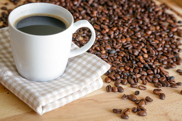 Coffee grains with white cup on coffee on wooden table, natural light