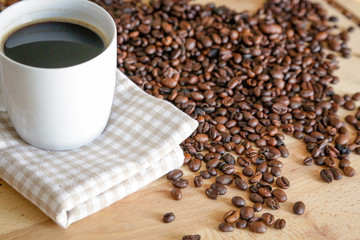 Coffee grains with white cup on coffee on wooden table, natural light