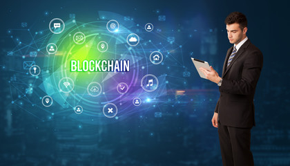 Businessman thinking in front of technology related icons and BLOCKCHAIN inscription, modern technology concept