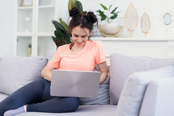 Beautiful young mother uses a laptop and smiling while sitting on sofa at home