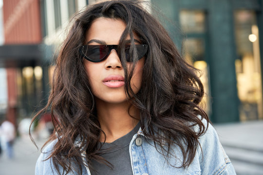 Confident Young Mixed Race African Gen Z Girl Wearing Stylish Sunglasses Standing On Urban City Street Looking At Camera, Portrait. Afro American Ethnic Woman In Trendy Glasses Closeup Face Headshot.