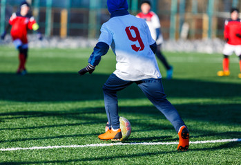 Boys in white red sportswear running on soccer field with snow on background. Young footballers dribble and kick football ball in game. Training, active lifestyle, sport, children winter activity 